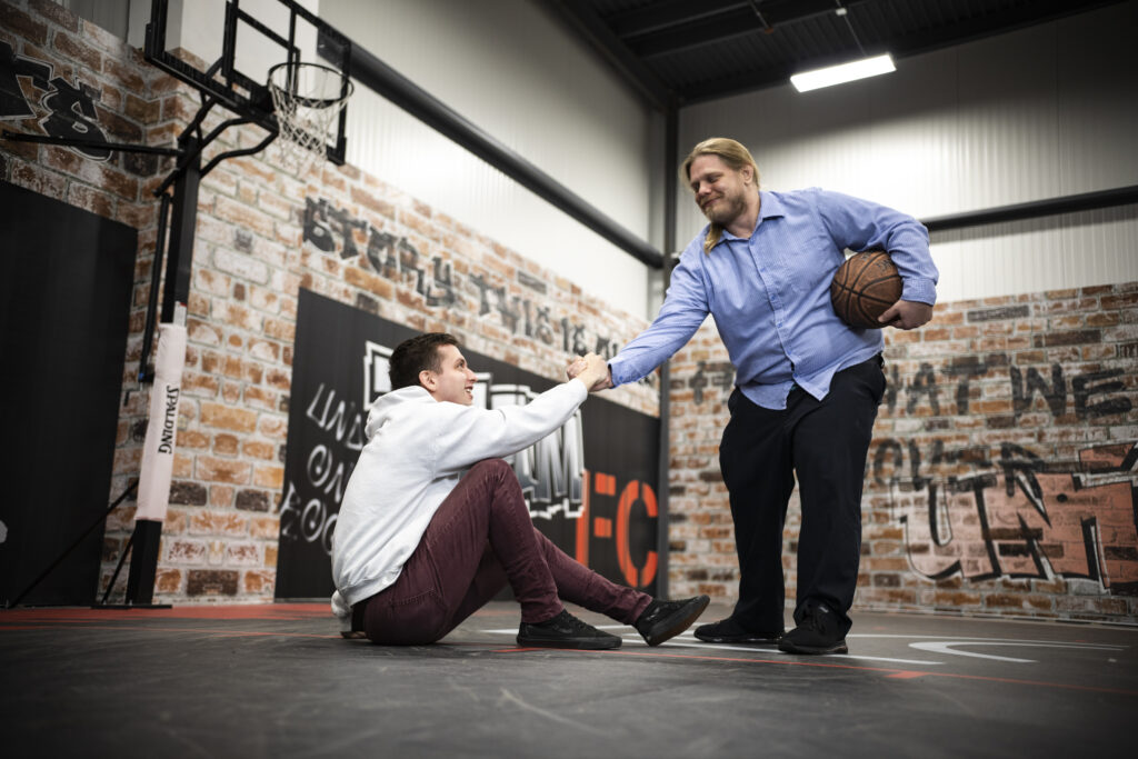 An employee helps another up on the basketball court