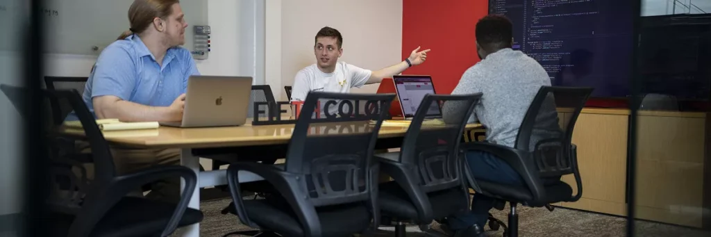 Three team members gathered around the meeting table to discuss what website maintenance is.